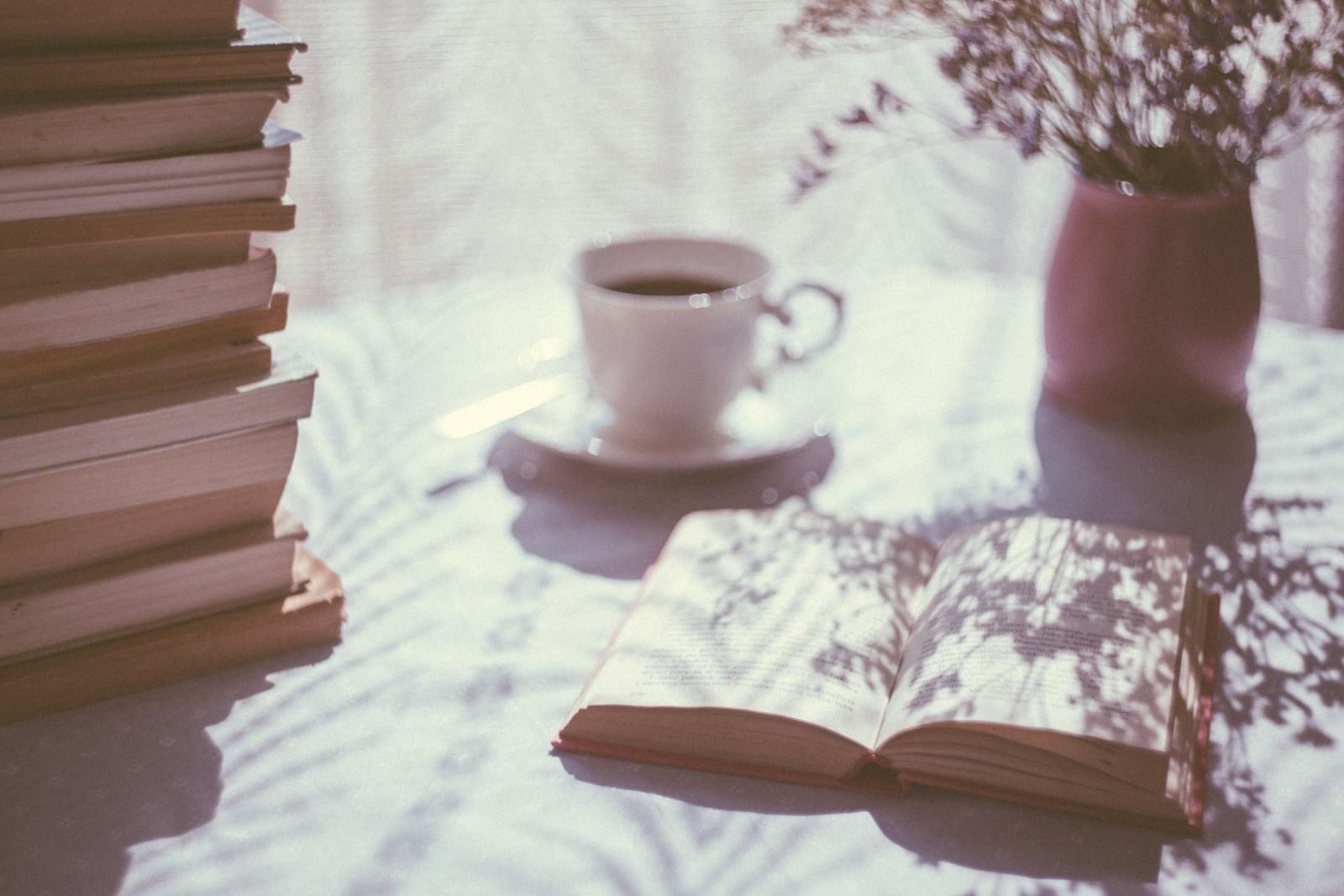 Книги, чаша и цветя на светла маса с меки сенки